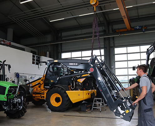 hallenkran zwei maenner heben anbau geraet mit kran auf traktor