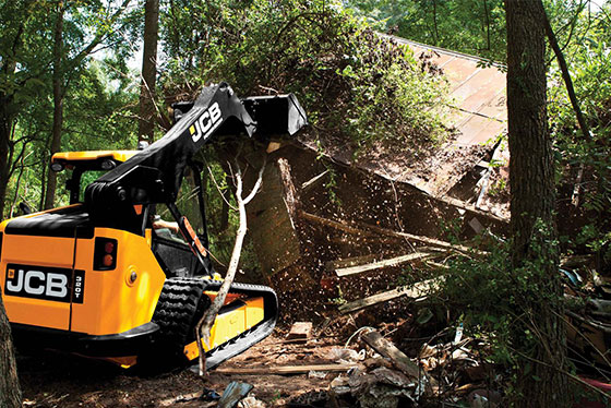 jcb kompaktraupenlader in gelb im wald zerstört haus